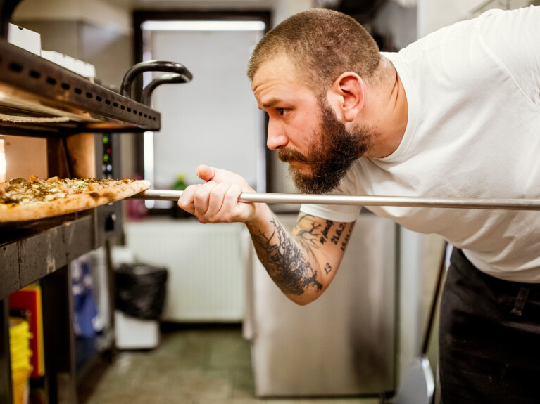 A chef putting pizza in a pizza oven.