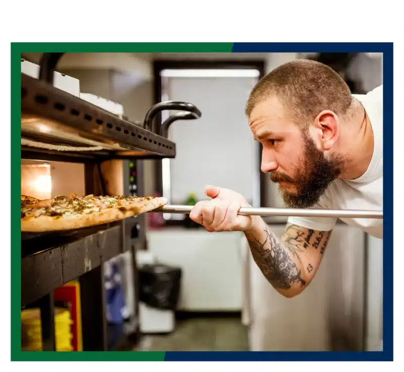 A chef putting pizza in a pizza oven.