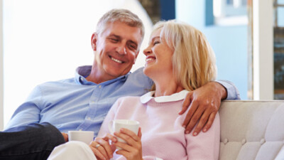 A man and a woman sitting on a couch, laughing and holding mugs.