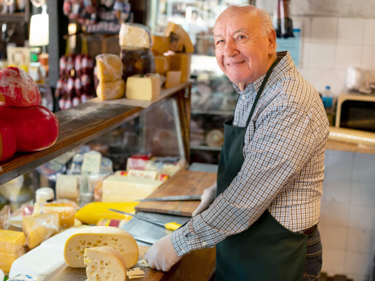 Man slicing cheese behind deli counter.