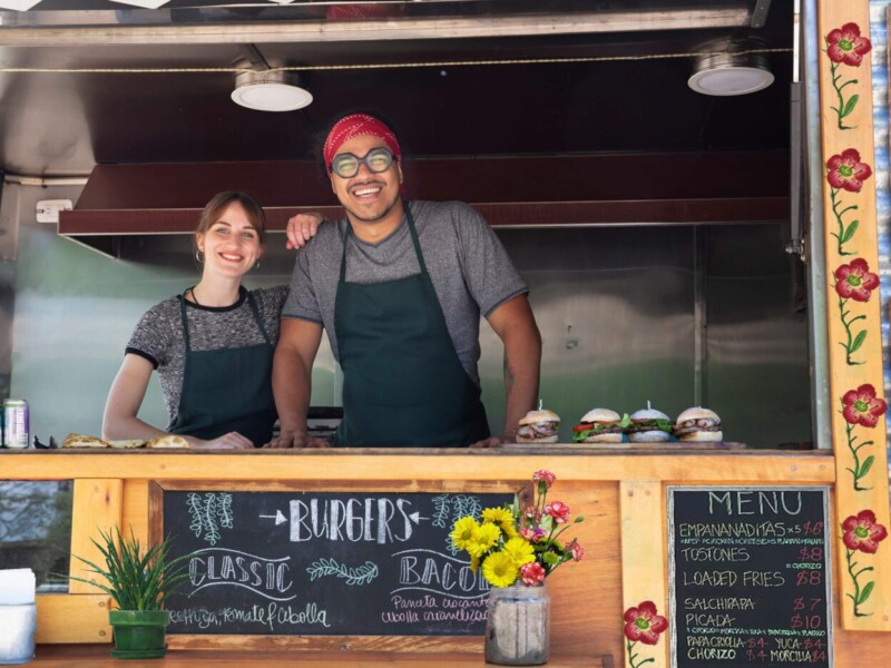 Woman and man smiling behind the counter of a food truck.