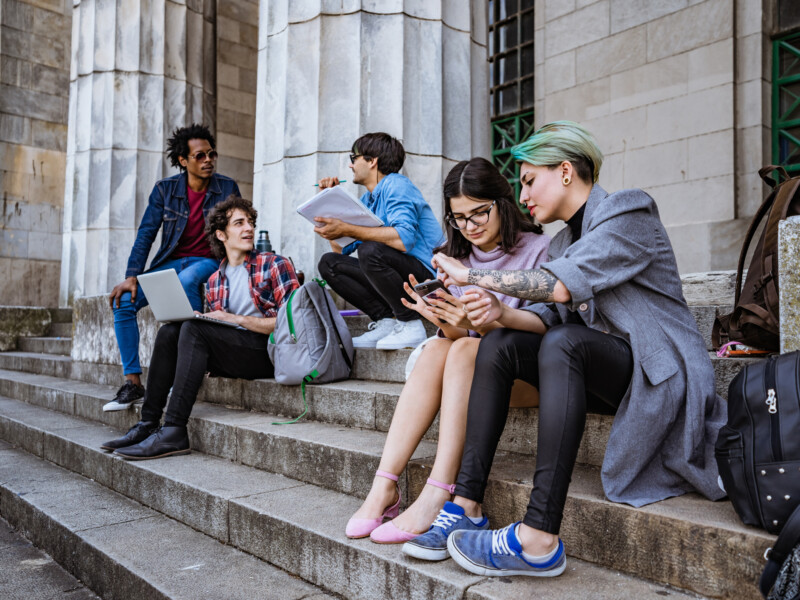 College students on the front steps of an academic building.