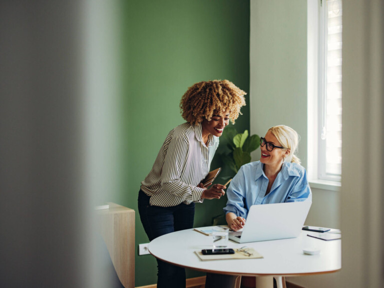 Two businesswomen working at a laptop discussing cash management solutions.