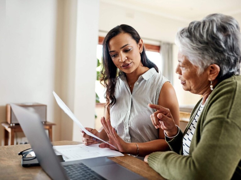 Two women looking at paperwork in front of a laptop.