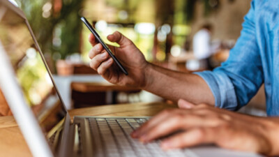 A man using his cell phone and his laptop simultaneously.