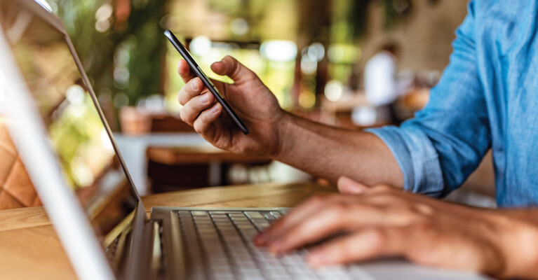 A man using his cell phone and his laptop simultaneously.