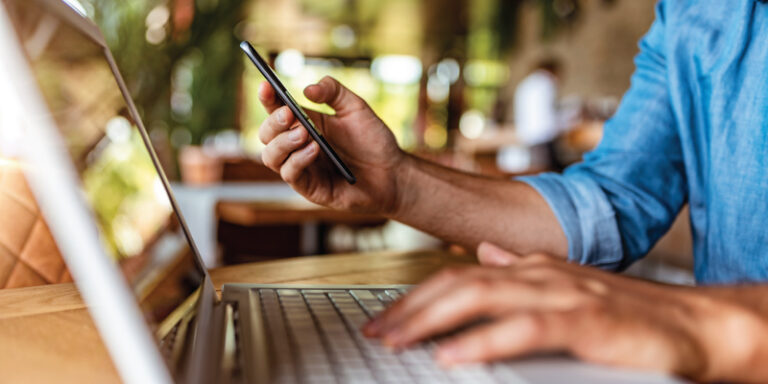 A man using his cell phone and his laptop simultaneously.