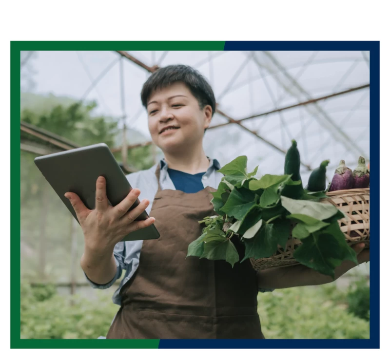 A woman holding a tablet and a basket of vegetables.