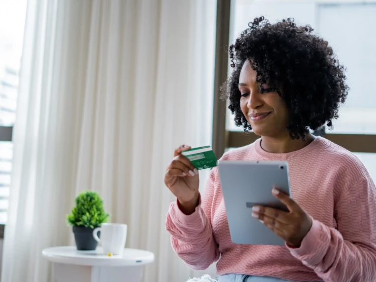 A woman holding a tablet and a debit card.