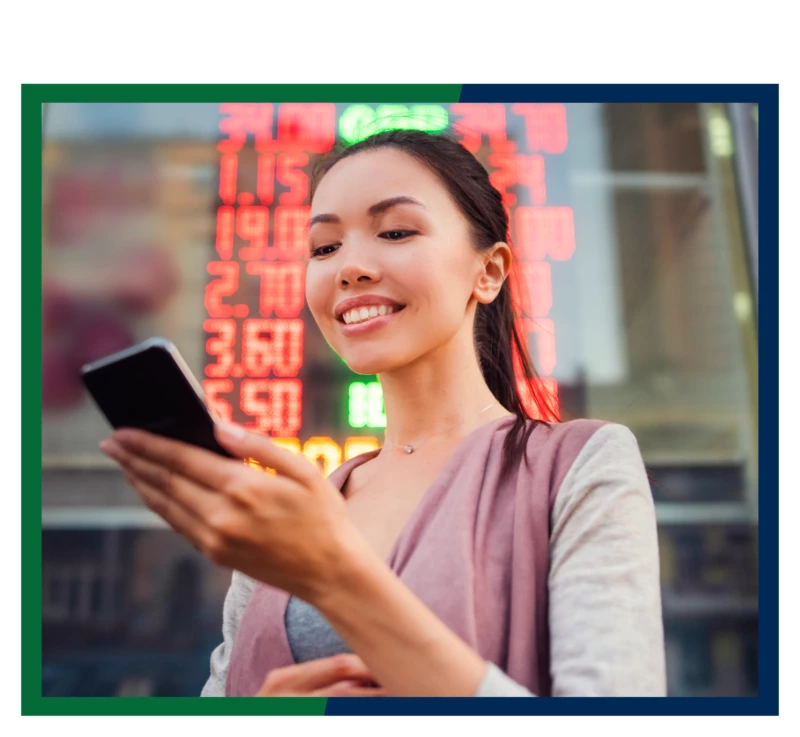 A woman looking at her cell phone, in front of a wall of stock rates.