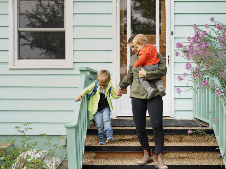 Woman with two children walking down front porch stairs.