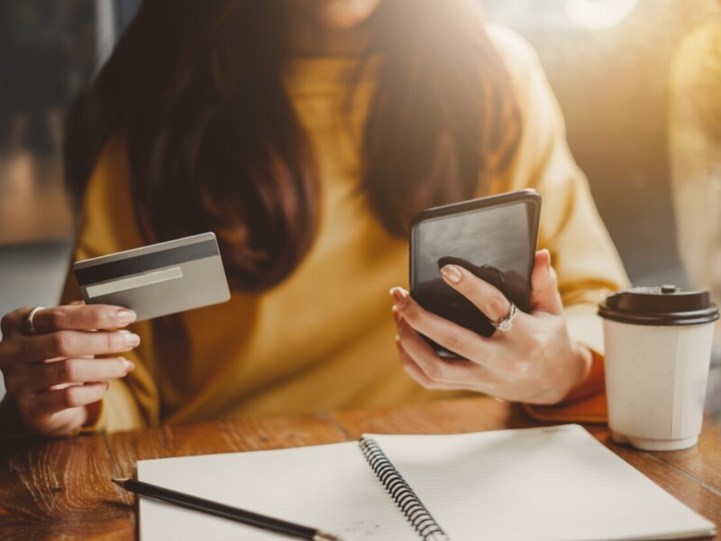 Woman holding a credit card in one hand and a cell phone in the other.